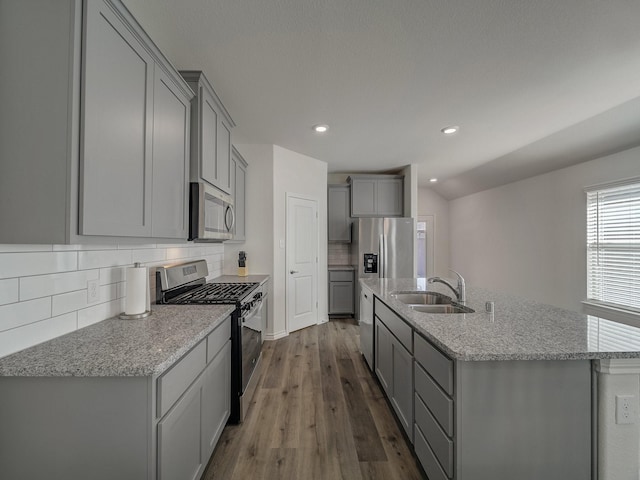 kitchen featuring an island with sink, sink, backsplash, stainless steel appliances, and light stone countertops