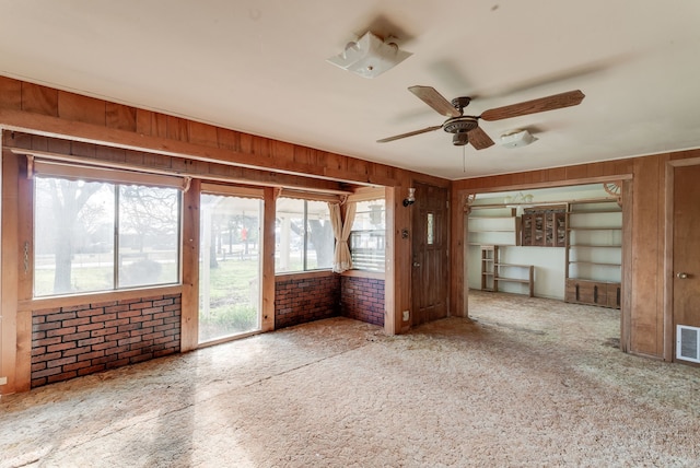 unfurnished living room featuring ceiling fan, brick wall, carpet flooring, and wood walls