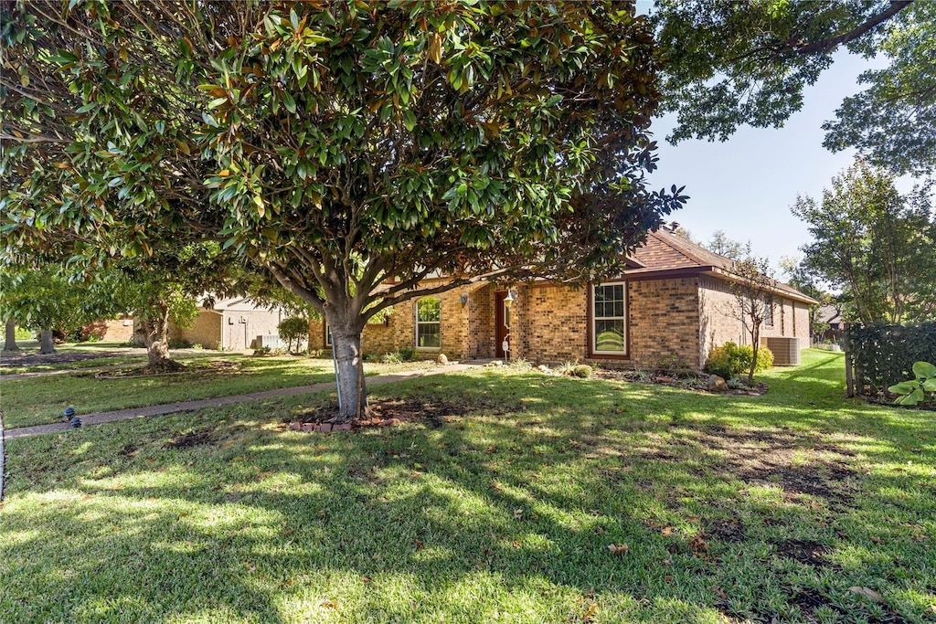 view of property hidden behind natural elements featuring central air condition unit and a front lawn