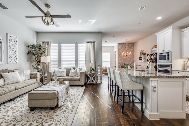 living room with dark hardwood / wood-style flooring and ceiling fan with notable chandelier