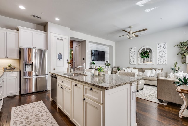 kitchen with sink, appliances with stainless steel finishes, dark hardwood / wood-style flooring, light stone countertops, and a kitchen island with sink