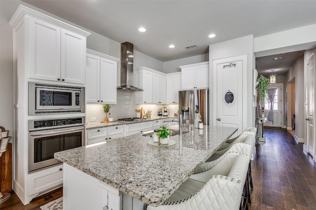 kitchen with appliances with stainless steel finishes, a kitchen breakfast bar, a large island with sink, and wall chimney range hood