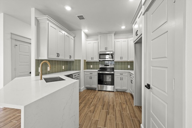 kitchen with sink, stainless steel appliances, tasteful backsplash, white cabinets, and kitchen peninsula