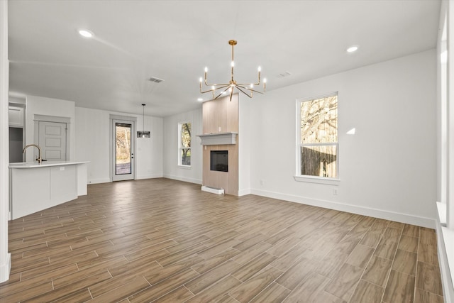 unfurnished living room featuring a healthy amount of sunlight, sink, and a notable chandelier