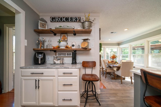 bar featuring white cabinetry, crown molding, and a textured ceiling