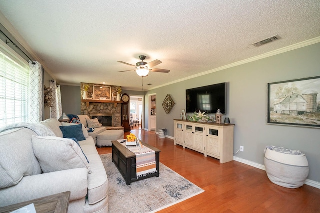 living room with crown molding, ceiling fan, a textured ceiling, dark hardwood / wood-style flooring, and a stone fireplace