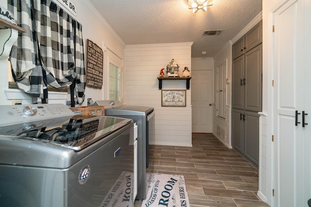 laundry room featuring wooden walls, cabinets, washing machine and clothes dryer, dark wood-type flooring, and a textured ceiling