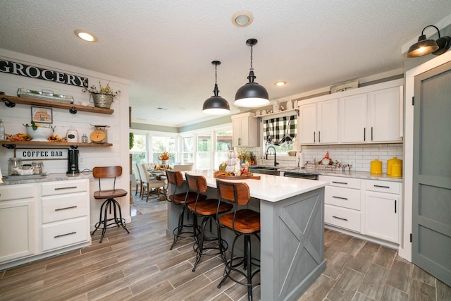 kitchen featuring decorative light fixtures, white cabinets, a kitchen breakfast bar, a center island, and a textured ceiling