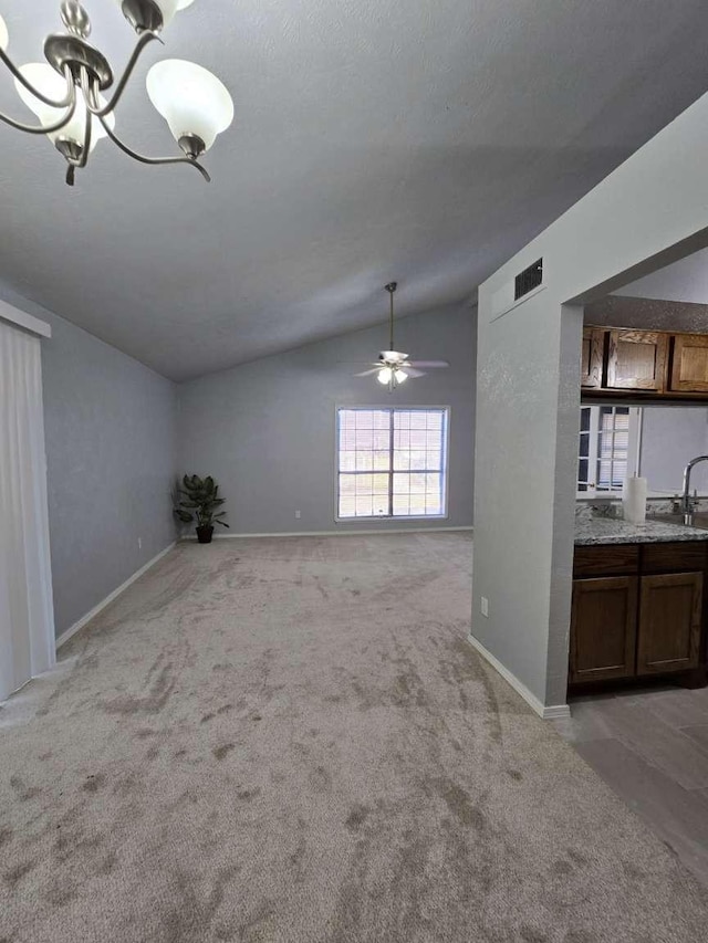 unfurnished living room featuring ceiling fan with notable chandelier, sink, vaulted ceiling, and light carpet