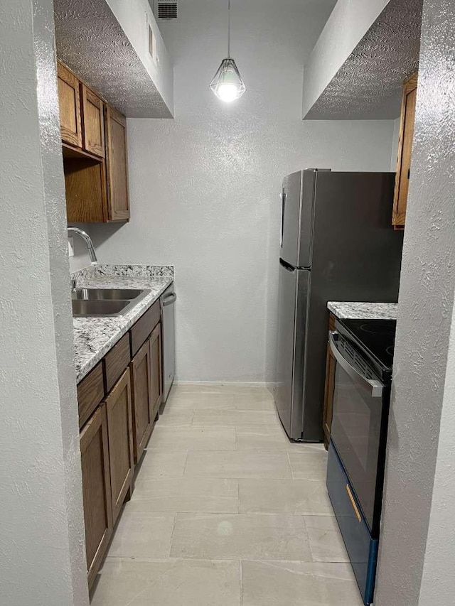 kitchen featuring sink, light stone countertops, hanging light fixtures, and appliances with stainless steel finishes