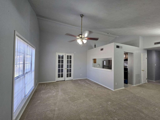 unfurnished living room with ceiling fan, high vaulted ceiling, carpet, a textured ceiling, and french doors