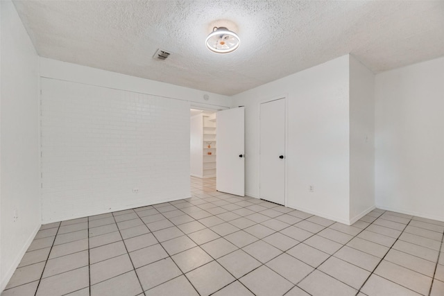 tiled spare room with brick wall and a textured ceiling