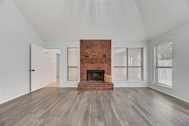 unfurnished living room with a brick fireplace, high vaulted ceiling, and light wood-type flooring