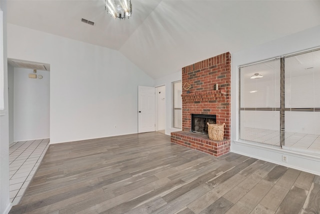 unfurnished living room featuring wood-type flooring, a brick fireplace, and lofted ceiling