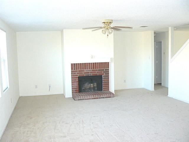 unfurnished living room featuring ceiling fan, light carpet, and a brick fireplace