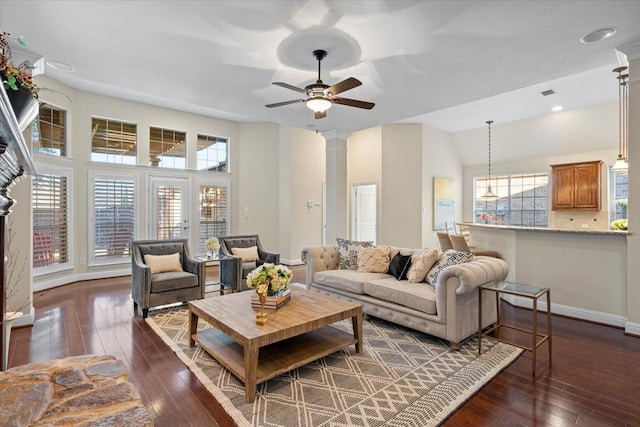 living room with dark wood-type flooring, ceiling fan, and ornate columns