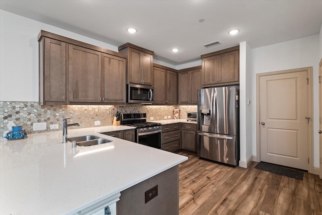 kitchen featuring sink, decorative backsplash, kitchen peninsula, and appliances with stainless steel finishes