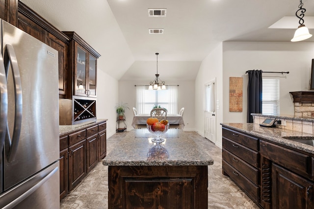 kitchen with stainless steel fridge, hanging light fixtures, a center island, dark brown cabinetry, and vaulted ceiling