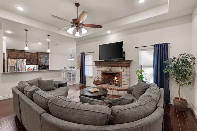 living room with ceiling fan, a fireplace, a raised ceiling, and a healthy amount of sunlight