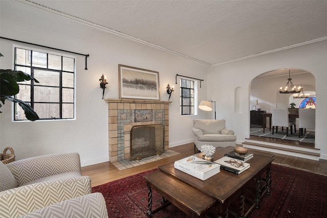 living room with a fireplace, wood-type flooring, a chandelier, crown molding, and a textured ceiling