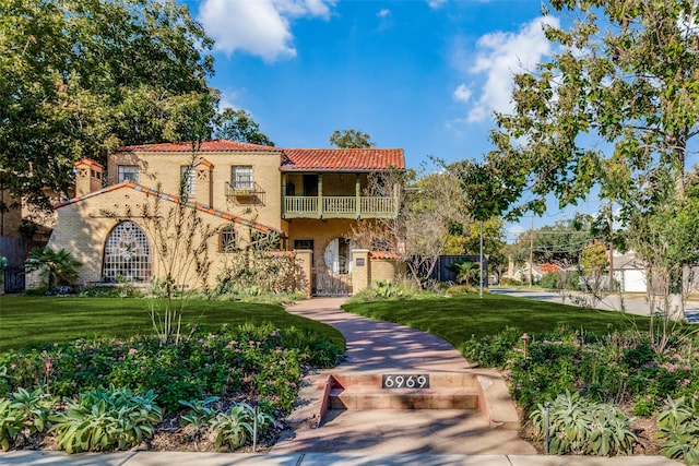 mediterranean / spanish-style home with a front lawn and a balcony