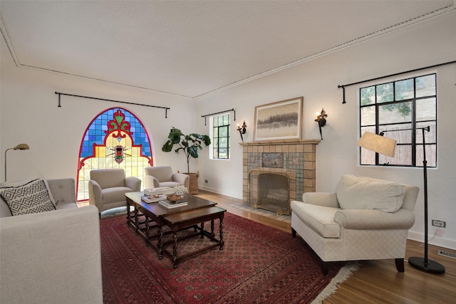 living room featuring a tiled fireplace, wood-type flooring, and crown molding