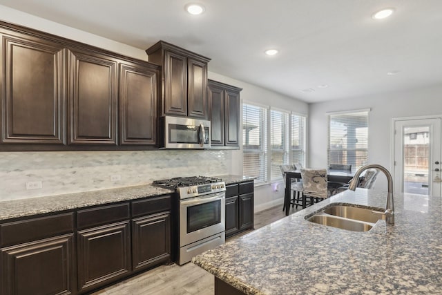 kitchen with decorative backsplash, light wood-style flooring, stainless steel appliances, dark brown cabinets, and a sink