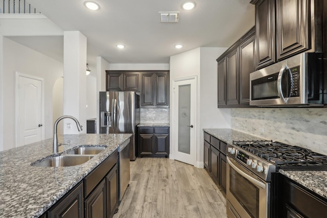 kitchen featuring appliances with stainless steel finishes, a sink, light wood-style flooring, and dark stone countertops