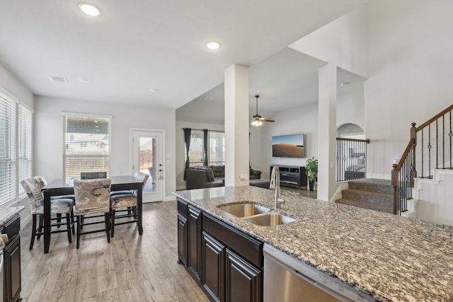 kitchen with open floor plan, a sink, stainless steel dishwasher, and light stone countertops