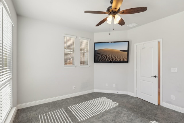 empty room featuring a ceiling fan, visible vents, dark carpet, and baseboards