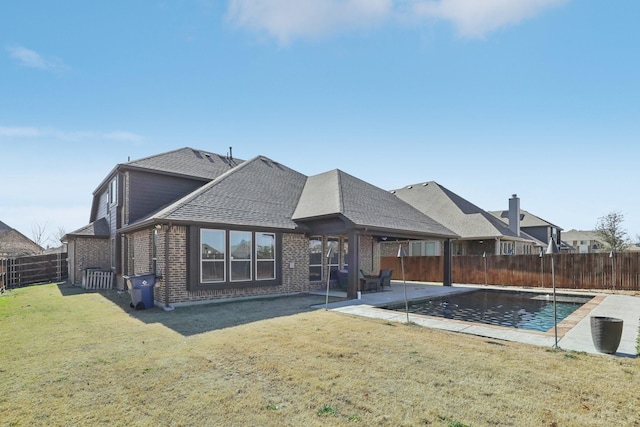 rear view of house featuring a fenced backyard, brick siding, roof with shingles, a lawn, and a patio area