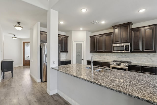 kitchen featuring tasteful backsplash, appliances with stainless steel finishes, a sink, dark stone countertops, and light wood-type flooring