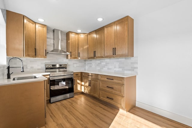 kitchen with wall chimney range hood, sink, tasteful backsplash, stainless steel range with electric cooktop, and light wood-type flooring