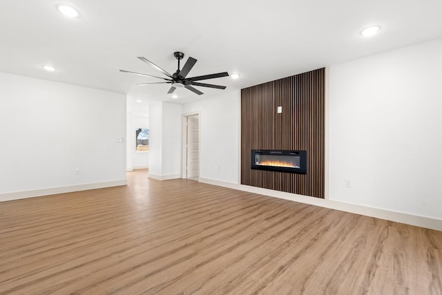 unfurnished living room with ceiling fan, a large fireplace, and light hardwood / wood-style flooring