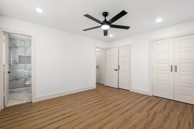 unfurnished bedroom featuring hardwood / wood-style floors, connected bathroom, multiple closets, and ceiling fan