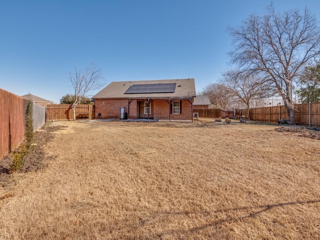 rear view of property featuring a yard and solar panels