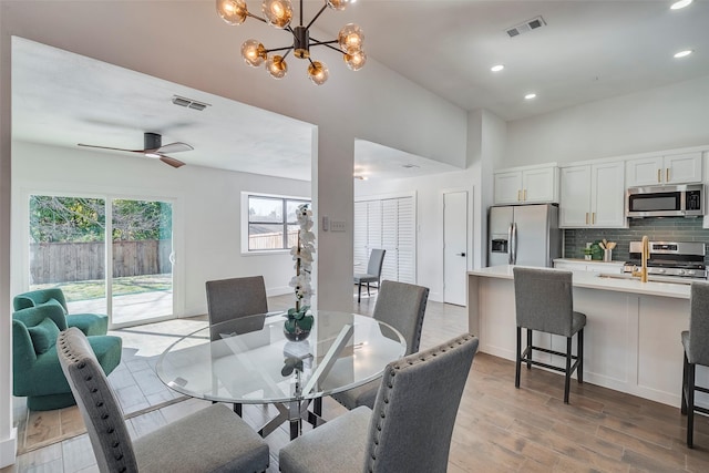 dining room with ceiling fan with notable chandelier and light hardwood / wood-style floors