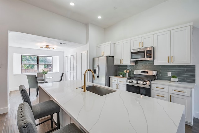 kitchen featuring sink, white cabinets, stainless steel appliances, light stone countertops, and a center island with sink