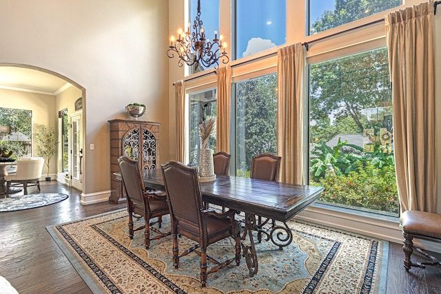 dining room featuring a towering ceiling, dark wood-type flooring, ornamental molding, and a chandelier