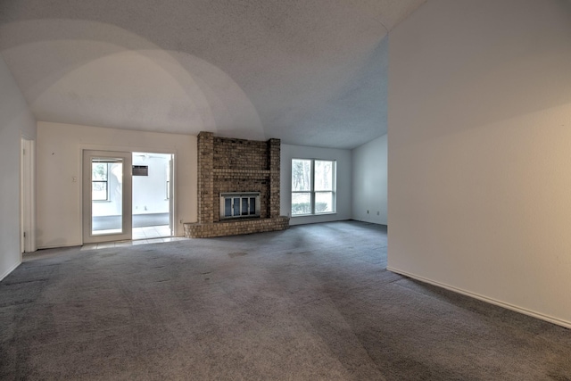 unfurnished living room with dark colored carpet, vaulted ceiling, a healthy amount of sunlight, and a fireplace