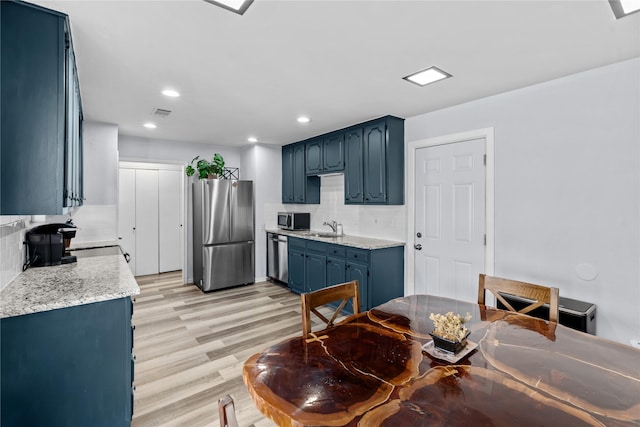 kitchen with sink, decorative backsplash, stainless steel appliances, blue cabinetry, and light hardwood / wood-style flooring