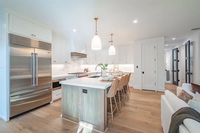 kitchen with pendant lighting, sink, premium range hood, white cabinetry, and built in fridge