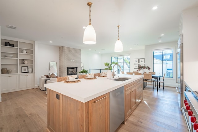 kitchen featuring sink, decorative light fixtures, a brick fireplace, appliances with stainless steel finishes, and a kitchen island with sink