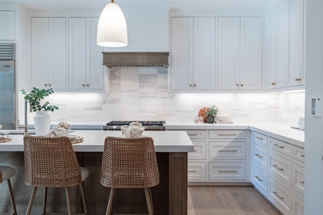 kitchen featuring white cabinetry, decorative light fixtures, a breakfast bar, and backsplash