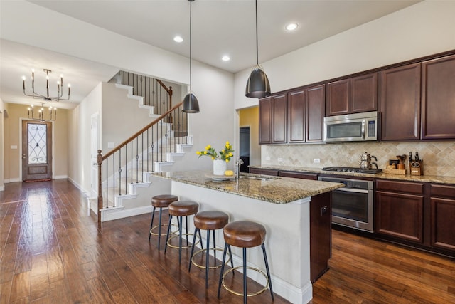 kitchen with pendant lighting, light stone counters, an island with sink, and appliances with stainless steel finishes