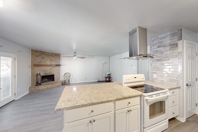 kitchen with a brick fireplace, white electric range, light stone countertops, and island exhaust hood