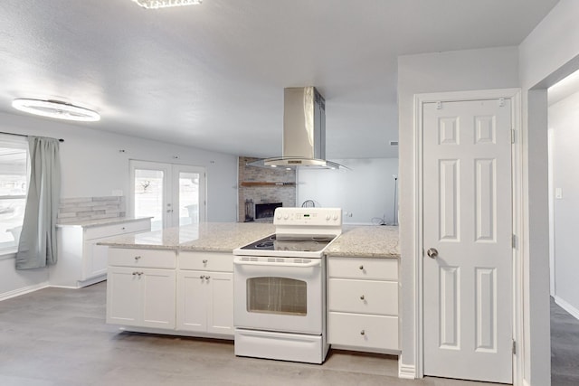 kitchen with white range with electric stovetop, white cabinets, island exhaust hood, light stone counters, and a brick fireplace