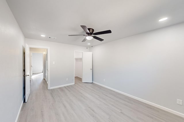 unfurnished bedroom featuring a spacious closet, light hardwood / wood-style floors, a closet, and ceiling fan