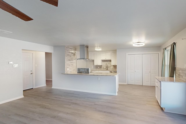 kitchen with wall chimney range hood, sink, light stone counters, light hardwood / wood-style floors, and white cabinets