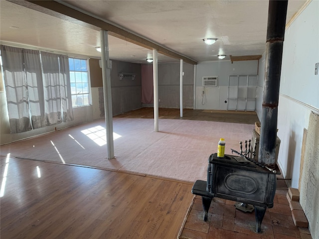 basement with hardwood / wood-style flooring, an AC wall unit, and a wood stove